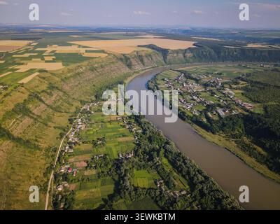 Ein Weitwinkelblick aus der Luft fängt den Fluss Dniester ein, der sich durch die ländliche Landschaft der Ukraine schlängelt, flankiert von landwirtschaftlichen Feldern und kleinen Dörfern Stockfoto