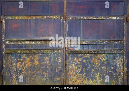 Alte, Rostfreie Stahltore. Nahaufnahme von stark verwittertem rostigem Stahltor mit abblätternder Farbe und industrieller Textur. Stockfoto
