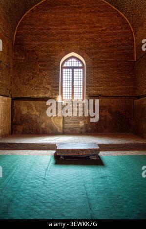 Vertikale symmetrische Aufnahme einer Innenhalle in der Blauen Moschee. Ein großes bogenförmiges Fenster mit Holzgittergitter beleuchtet den Raum Stockfoto