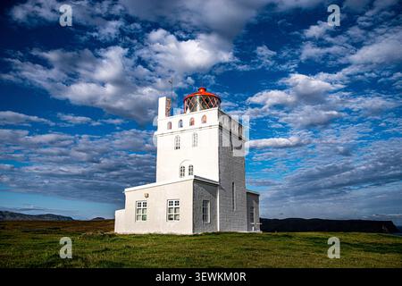 Der historische, weiße Leuchtturm in Form eines Dyrholaey-Schlosses mit seiner berühmten roten Spitze, der auf einem grünen Hügel unter einem wunderschönen bewölkten Himmel in Südisland steht. Stockfoto