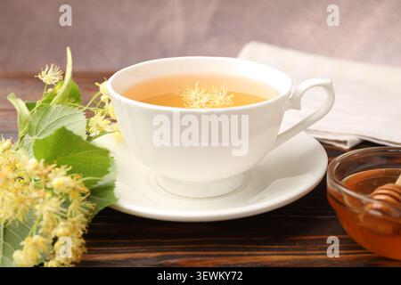 Köstlicher Lindentee in Tasse, Honig, Blätter und Blumen auf Holztisch, Nahaufnahme Stockfoto