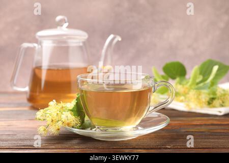 Köstlicher Lindentee in Glasbecher, Blätter und Blumen auf Holztisch, Nahaufnahme Stockfoto