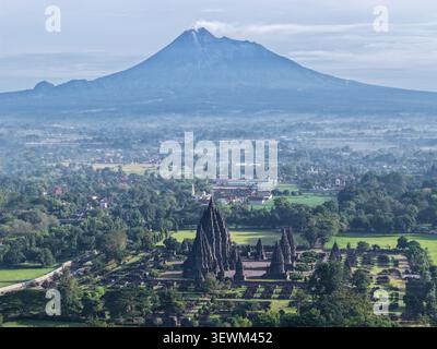Aus der Vogelperspektive auf den Prambanan Tempel mit Steintürmen und üppigem Grün, mit dem Vulkan Merapi im Hintergrund in Kecamatan Prambanan, Daerah Istime Stockfoto