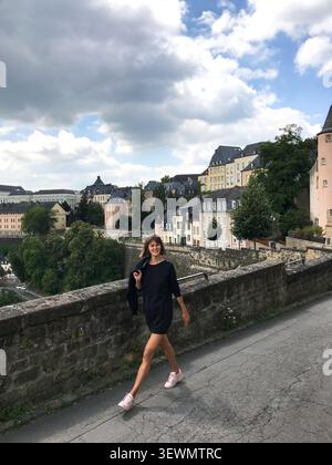Stylische Frau in einem kurzen schwarzen Kleid, die entlang eines malerischen Aussichtspunktes geht, der über das malerische Tal blickt. Das elegante Reiseporträt Stockfoto