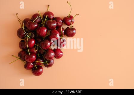 Frische rote Kirschen in Herzform auf weichem pfirsichfarbenem Hintergrund mit Kopierraum. Einfaches Essen Stillleben mit süßer Sommerstimmung. Stockfoto