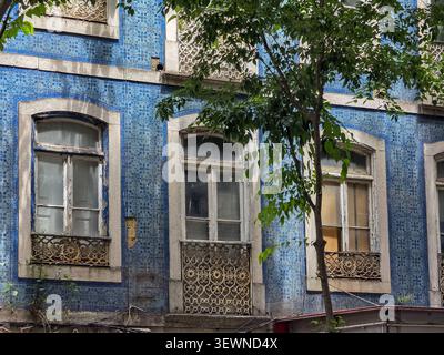 Verwittertes Azulejo-überdachtes Gebäude hinter Stadtbäumen in Lissabon, Portugal Stockfoto