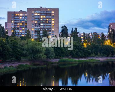 Städtische Wohngebäude entlang des Rusanivsky-Kanals in Kiew, die sich in der Dämmerung auf dem ruhigen Wasser spiegeln und ein Gefühl von städtischem Wohnen und Ev schaffen Stockfoto