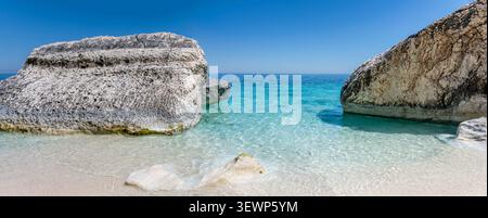 Große Panoramalandschaft mit Felsblöcken im flachen, transparenten Wasser an einem kleinen Sandstrand in der Bucht Cala Mariolo am Mittelmeer, s Stockfoto