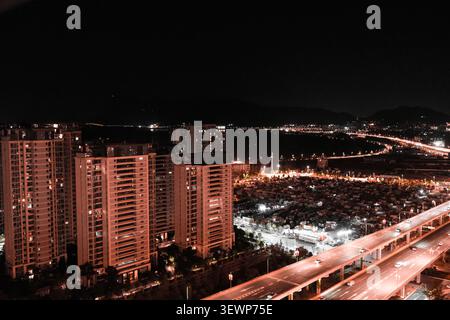 Blick auf die Stadt bei Nacht mit hohen Apartmentgebäuden, hellen Straßenlaternen und einer geschäftigen Skyline von oben unter dunklem Himmel. Stockfoto