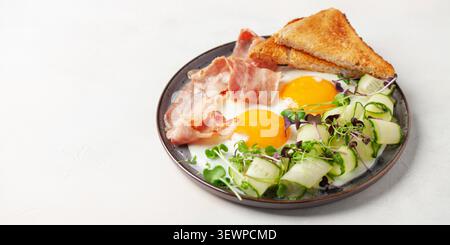 Kontinentales Frühstück - Eier, Speck, Mikrogemüse und Gurkenscheiben auf einem Teller auf dem Tisch. Gesundes Frühstück. Stockfoto