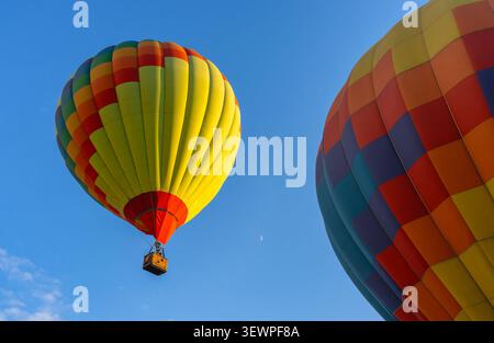 Leuchtende bunte Heißluftballons fliegen am klaren blauen Himmel mit einem Halbmond. Stockfoto