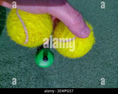 Ein aus der Perspektive der ersten Person geschossener Blick auf eine Hand, die zwei unscharfe Tennisbälle über einer strukturierten grünen Spielfläche hält. Eine Flasche mit grünem Sportgetränk Stockfoto