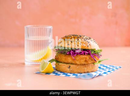 Fisch-Burger mit zerkrümeltem Fischfilet und Rotkohl auf einem knusprigen Brötchen serviert auf einem Teller vor farbigem Hintergrund Stockfoto