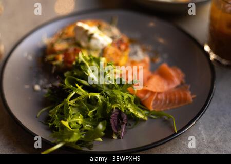 Detaillierte Nahaufnahme eines Brunch-Gerichts im Restaurant mit Räucherlachs, einer frischen grünen Salatmischung und einem herzhaften Pfannkuchen mit Frischkäse Stockfoto