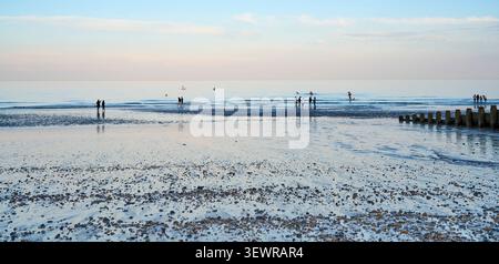 Badegäste am Strand und im Meer bei Sonnenuntergang im Juni mit gedämpften Farben am Himmel dahinter Stockfoto