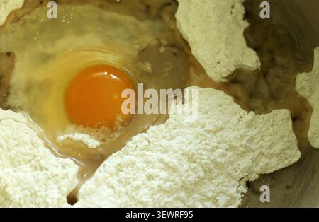Frisches Eigelb und weiß werden zu einem Haufen weißem Mehl vermischt, um die Zutaten zu einer perfekten Teigmischung zum Backen, Kochen oder Gebäck zu vermischen Stockfoto