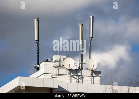 Mehrere Mobilfunkantennen und Satellitenschüsseln auf dem Dach des Gebäudes vor bewölktem Himmel Stockfoto