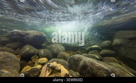 Unterwasserblick in einem wilden Schweizer Bergfluss mit Blick auf die turbulente Oberfläche unter einem kleinen natürlichen Wasserfall, mit starker Strömung, Blasen Stockfoto