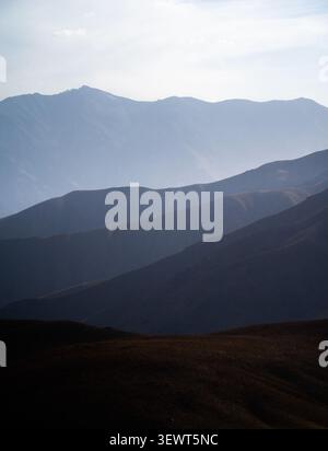 Blick auf den Arashan-See, umgeben von geschichteten Bergketten und sanften Hügeln unter einem trüben Himmel im Pop District, Namangan Region, Usbekistan. Stockfoto