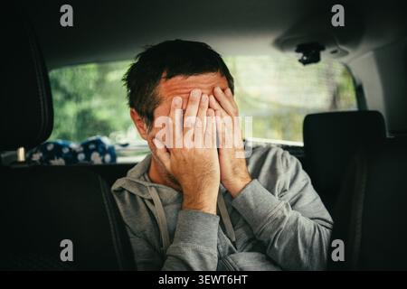 Ein Mann mittleren Alters sitzt in einem Auto mit dem Kopf auf der Hand, erscheint müde, gestresst und tief in Gedanken. Selektiver Fokus. Stockfoto
