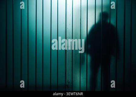 Geheimnisvoller Schatten hinter Milchglaspaneelen, der Isolation und Spannung sowie selektiven Fokus vermittelt Stockfoto