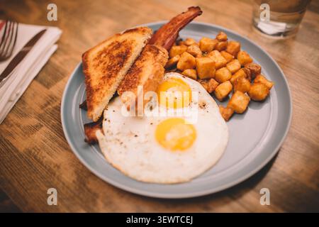 Frühstücksteller mit zwei Spiegeleiern auf Toast, Kartoffeln und Speck Stockfoto