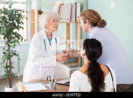 Ein freundlicher älterer Arzt schüttelt dem jungen Paar die Hand Stockfoto