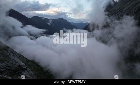 Atmosphärischer Blick auf die dichten niedrigen Wolken, die bei Sonnenaufgang durch das dramatische Trollstigen-Bergtal fließen, umgeben von hohen Gipfeln, zerklüftete C Stockfoto