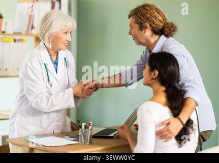 Ein freundlicher älterer Arzt schüttelt dem jungen Paar die Hand Stockfoto