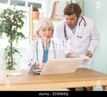 Ältere Frau und erwachsene männliche Ärzte arbeiten am Laptop in der Arztpraxis Stockfoto