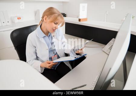 Ärztin telefoniert und prüft medizinische Unterlagen Stockfoto