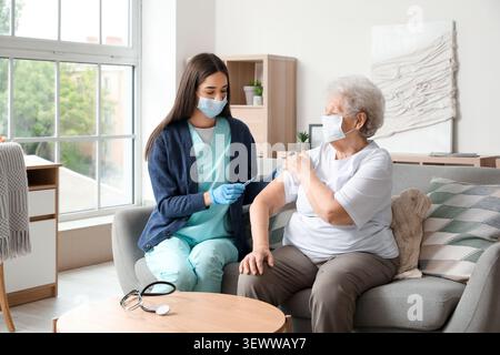 Junge Krankenschwester geimpft Seniorinnen zu Hause Stockfoto