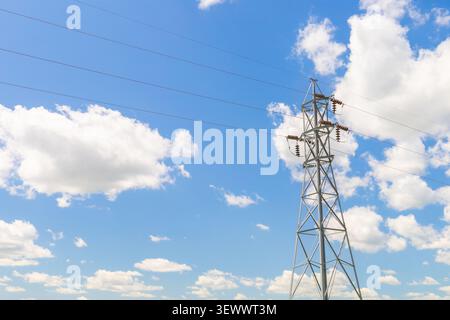 Hochspannungs-Übertragungsturm mit Stromleitungen unter blauem Himmel mit Wolken. Energieinfrastruktur, Stromnetz und Versorgungsunternehmen Stockfoto