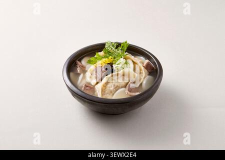 Traditionelle koreanische Knödelsuppe mandu Guk serviert in einer schwarzen Schüssel mit Eiergarnitur und grüner Zwiebel auf hellgrauem Hintergrund, koreanisches Komfortessen Pho Stockfoto