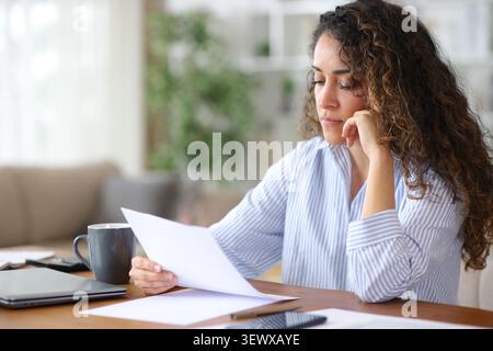 Konzentrierter erwachsener Telearbeiter, der Papierformulare sorgfältig liest und zu Hause arbeitet Stockfoto