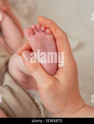 Ein herzerwärmendes vertikales Makrofoto, das einen Moment einer Mutter feststellt, die die winzige, faltige Fußsohle ihres Neugeborenen massiert. Das Foto hat ein weiches Bild Stockfoto