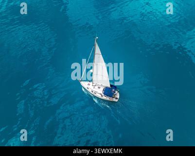 Von oben nach unten auf eine weiße Segelyacht, die durch das pulsierende türkisfarbene Meerwasser gleitet Stockfoto