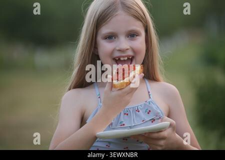 Glückliches Kind genießt hausgemachtes Brot mit Ajvar im Garten, authentischer Familienstil Stockfoto