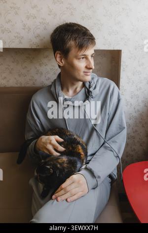 Junger Mann, der auf dem Sofa sitzt und Schildpattkater hält Stockfoto