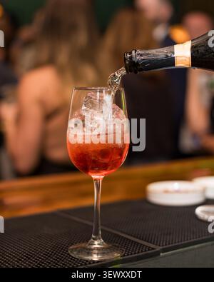 Gießen Sie Sekt in einen roten Spritz-Cocktail Stockfoto