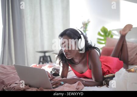 Frau mit Kopfhörern, die sich auf dem Bett mit Laptop entspannen Stockfoto
