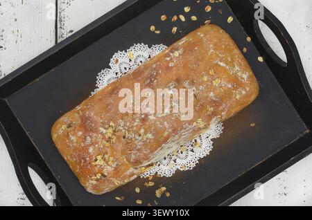 Essen von oben auf einem hölzernen Küchentisch. Frisch gebackenes, hausgemachtes Brot auf einem Holztablett. Lokaler, regionaler Geschmack. Vintage, weiße Serviette und Haferflocken. Stockfoto