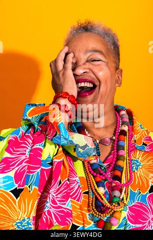 Schwarze Seniorin trägt moderne Kleidung Porträt auf Hintergrund - afroamerikanische Seniorin lacht unkontrolliert, während sie ihr Gesicht bedeckt Stockfoto