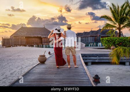 Ein romantisches Paar genießt den tropischen Sonnenuntergang auf einem Pier auf den Malediven Inseln während ihres Urlaubs Stockfoto