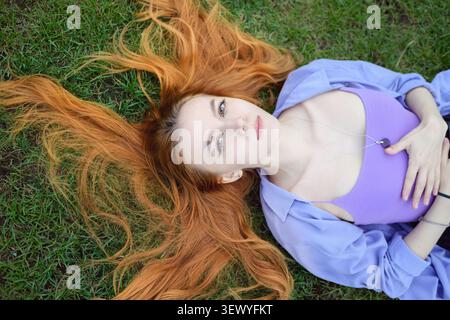 Rothaarige Frau im purpurpurnen Outfit auf Gras liegend. Stockfoto