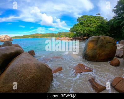 Tropischer Strand auf den Seychellen mit ikonischen Granitblöcken, die von ruhigen türkisfarbenen Meereswellen unter einem leuchtend blauen Himmel gewaschen werden und ein unberührtes sce schaffen Stockfoto