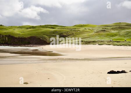 Ein Gezeitenstrom windet sich über eine weite Fläche aus hellem Sand unter grünen, dünenbedeckten Hügeln am Cliff Beach, Isle of Lewis, Outer Hebrides, Schottland Stockfoto