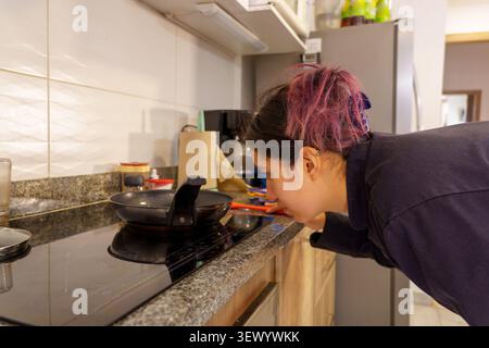 Frau, die hausgemachtes Essen zubereitet und das Aroma beim Kochen in einer modernen Küche überprüft Stockfoto