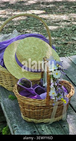 Strohhut mit Korb mit Lavendelblüten auf hölzernem Hintergrund Stockfoto