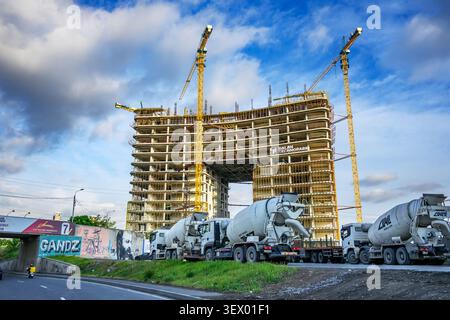 Große Baustelle mit Kränen und Betonwagen. Gebäudestruktur in Entwicklung. Blauer Himmel mit Wolken darüber. Straße und Grün bei Bas Stockfoto